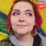 redhaired woman with septum piercing and red eyeshadow wearing brass hoops with teeth